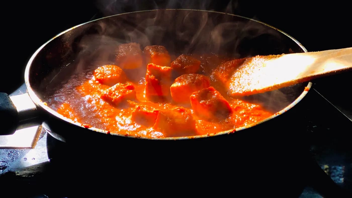 A curry base simmering in a pan on the stove, stirred with a spoon