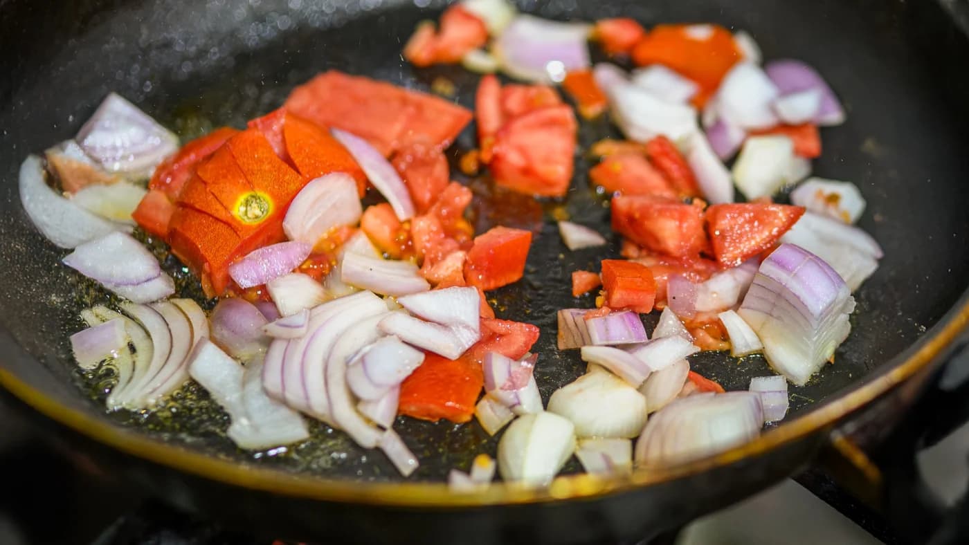 Chopped onions and tomatoes softening in a pan on a gas stove