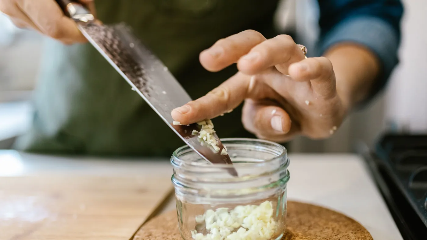 Chopped garlic being spooned into a glass storage jar
