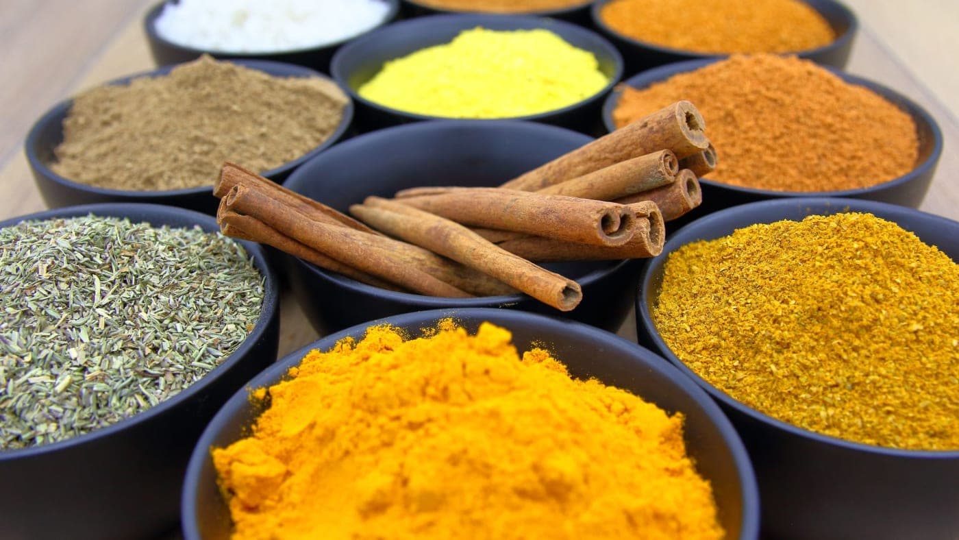 Ground spices in separate bowls with whole cinnamon sticks between them