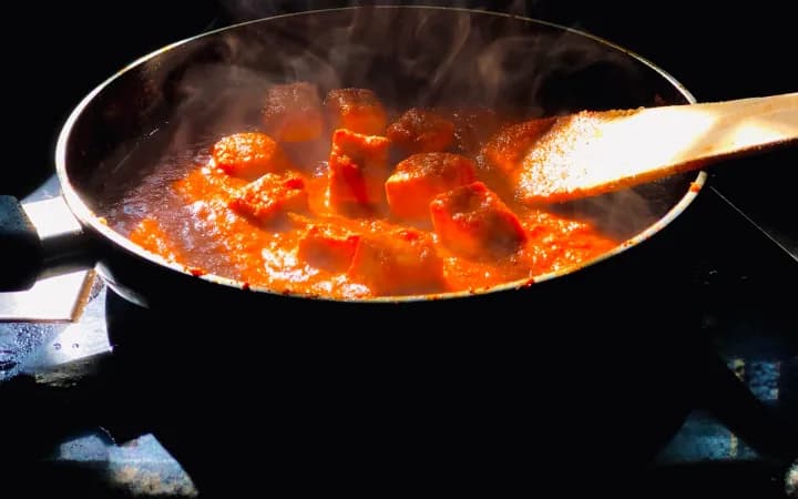 A curry base simmering in a pan on the stove, stirred with a spoon