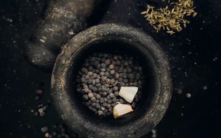 A stone mortar and pestle with whole peppercorns and garlic, seen from above